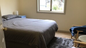 A bedroom with a bed, a wooden floor, a window, a chair, and a rug.