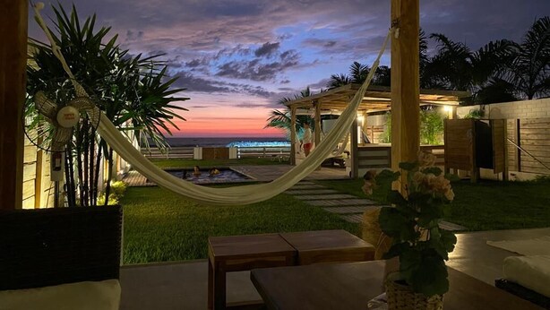 Une terrasse extérieure avec un hamac, une piscine et une vue sur le coucher du soleil.