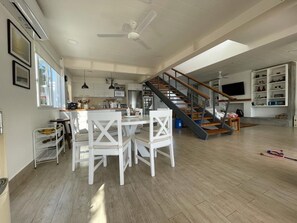 A spacious living area with a dining table, chairs, a staircase, and a TV mounted on the wall.