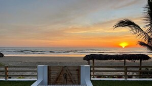 Une porte en bois qui mène à une plage offrant une vue sur le coucher de soleil.