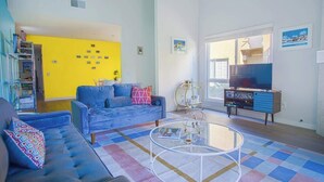 A living room with a sofa, coffee table, TV stand, and a yellow wall. - Stylish 2BR+Office, Big Pool, Pickleball and more (Palm Springs)