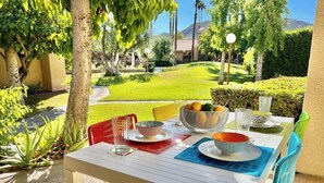 An outdoor dining area with a table set for two, surrounded by greenery and a view of a well-maintained lawn and distant mountains. - Stylish 2BR+Office, Big Pool, Pickleball and more (Palm Springs)