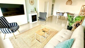 Un salon moderne comprenant un canapé, des fauteuils à rayures, une table basse, un téléviseur, une cheminée et un coin repas avec des chaises et une table.