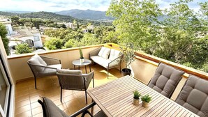 Un balcon ensoleillé avec une table en bois, deux chaises en osier, un canapé et une plante en pot.