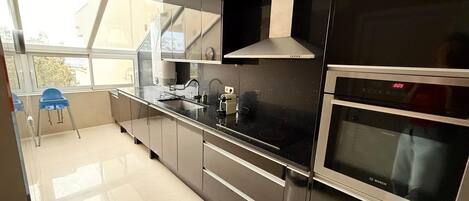 Una cocina moderna con encimera negra, electrodomésticos de acero inoxidable y ventana con vistas a una zona residencial.