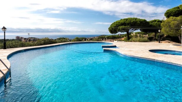 Une piscine d’un bleu éclatant, à bords incurvés, entourée d’une terrasse dallée et offrant une vue sur la mer et les bâtiments situés au loin.