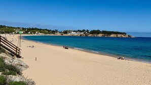 Une plage avec un escalier en bois descendant jusqu’au rivage, un ciel bleu dégagé et des bâtiments en arrière-plan.