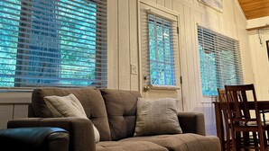 Una sala de estar con un sofá marrón, techo de madera y ventanas grandes con persianas.