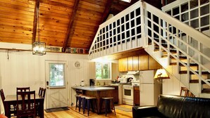 Un interior acogedor con zona de comedor, cocina y una escalera que sube a un nivel superior.