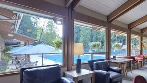 Un espacio interior amplio con grandes ventanales, una piscina visible al exterior y varias zonas de estar.