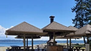 Zona de pabellones frente a la playa con varias estructuras de madera, algunas con bancos y mesas, que dan a una masa de agua.