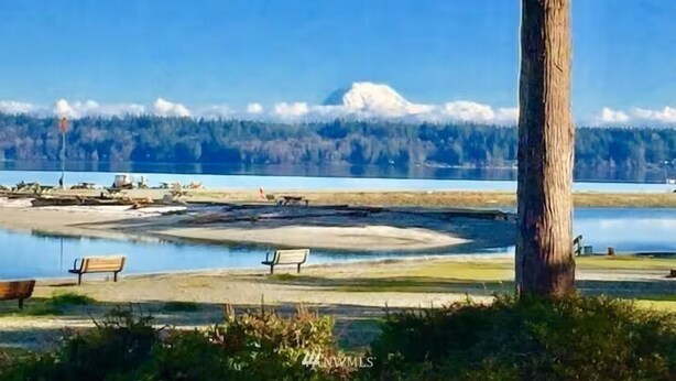 Vista de un lago con un banco, un árbol y una cadena montañosa distante.