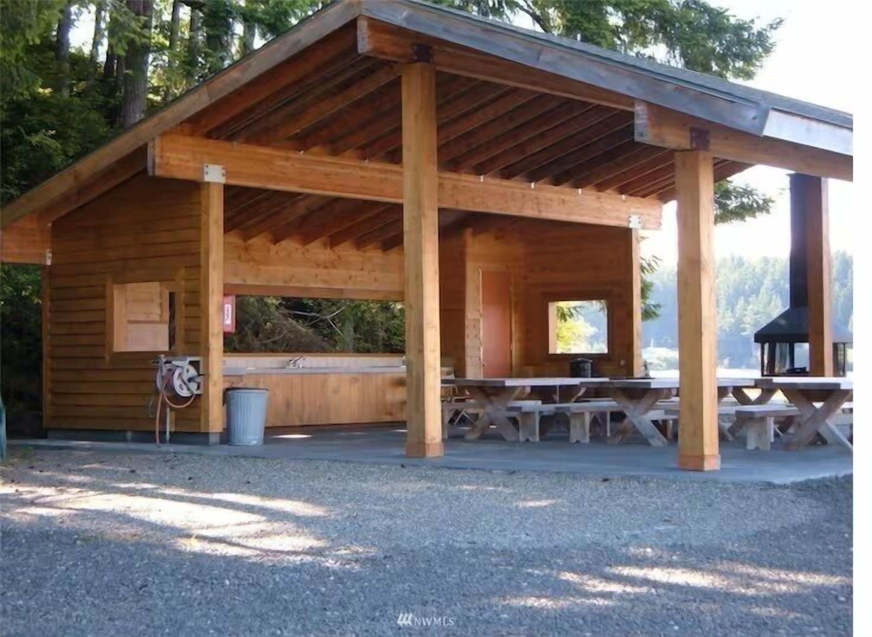 A wooden pavilion with a covered seating area, a trash bin, and a barbecue grill.