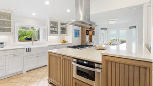 A modern kitchen with white cabinetry, a large island, stainless steel appliances, and a view of greenery outside. - 1001 E. Arctic - Out Of The Blue - Unique Outdoor Space- Luxury (Folly Beach)