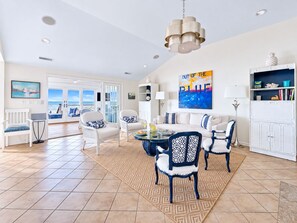 Un salon spacieux avec vue sur la mer, des meubles blancs et un grand tableau.