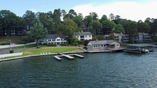 En fastighet vid sjön med en brygga, ett litet hus och flera fler våningar höga byggnader i bakgrunden.