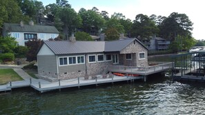 Una casa frente al agua con fachada de piedra, un muelle y un bote pequeño.