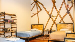 Ein Zimmer mit zwei Betten, Holzboden und einem Regal mit Handtüchern.