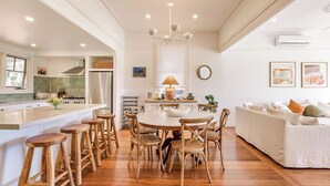 A modern kitchen with a central island, wooden stools, a dining table, and a white sofa. - Buttercup Farm Yallingup (Yallingup)