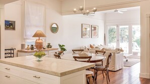 A spacious kitchen with a marble countertop, wooden chairs, and a dining table. There is a large window providing natural light and a view of the outdoors. - Buttercup Farm Yallingup (Yallingup)