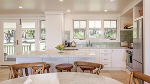 A modern kitchen with a large island, white cabinetry, and a view of the outdoors. - Buttercup Farm Yallingup (Yallingup)