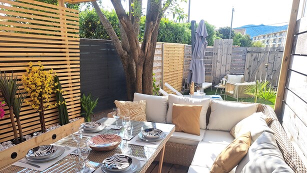 An outdoor patio with a dining table set for four, surrounded by a wicker sofa with cushions.