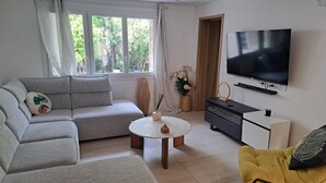 A living room with a sofa, a yellow chair, a TV, a small table, and a window with curtains.