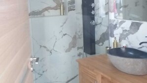 A bathroom with a marble wall, a wooden vanity, a large mirror, and a black towel rack.