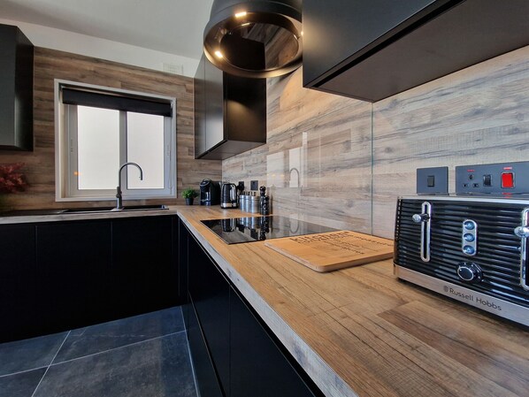 A modern kitchen with a built-in stove, a large window, and a wooden backsplash. - Eden Boutique Smart Home with Garage (San Pawl il-Baħar)