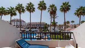 Ein Balkon mit Blick auf einen Pool, Liegestühle und ein Tisch mit einer Weinflasche.