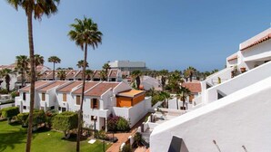 Ein Küstenhotel mit weißen Gebäuden, Palmen und freiem Blick auf das Meer.