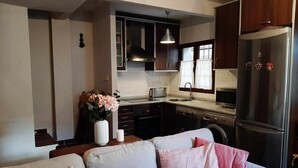 A compact living space with a kitchenette, a sofa with cushions, a vase with flowers, and a refrigerator.