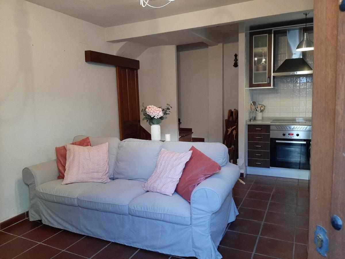 Una sala de estar con un sofá, un jarrón con flores y una cocina al fondo.