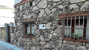 A stone building with a rustic appearance, featuring a window with metal bars and a small potted plant on the ledge.