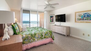 Un dormitorio con cama, ventilador de techo, televisor, cómoda y un cuadro.