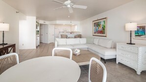 Una sala de estar amplia con un sofá blanco, una mesa de comedor con sillas, un aparador blanco y un ventilador de techo.