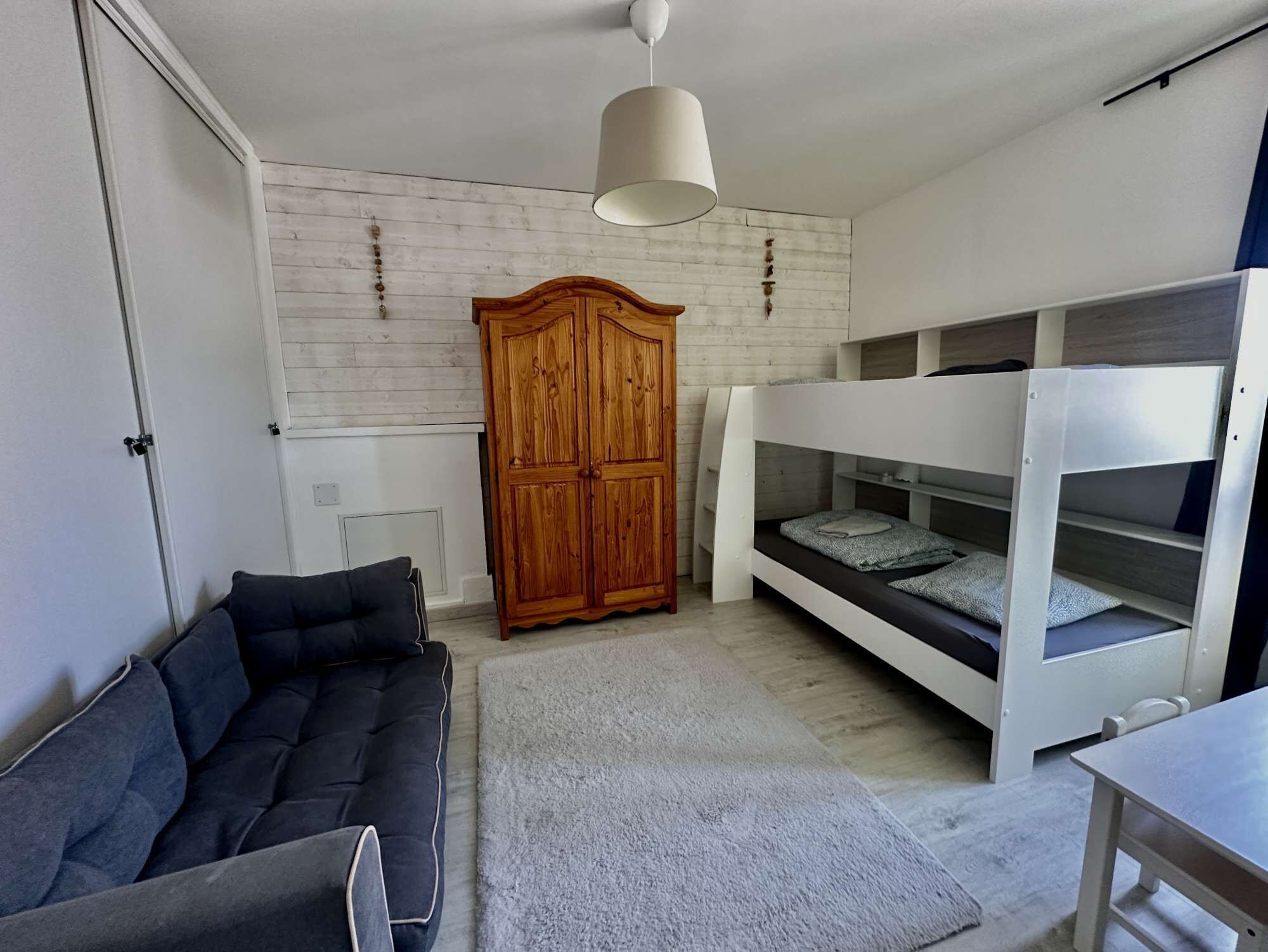 Een moderne slaapkamer met een stapelbed, een houten garderobe, een bank en een hanglamp.