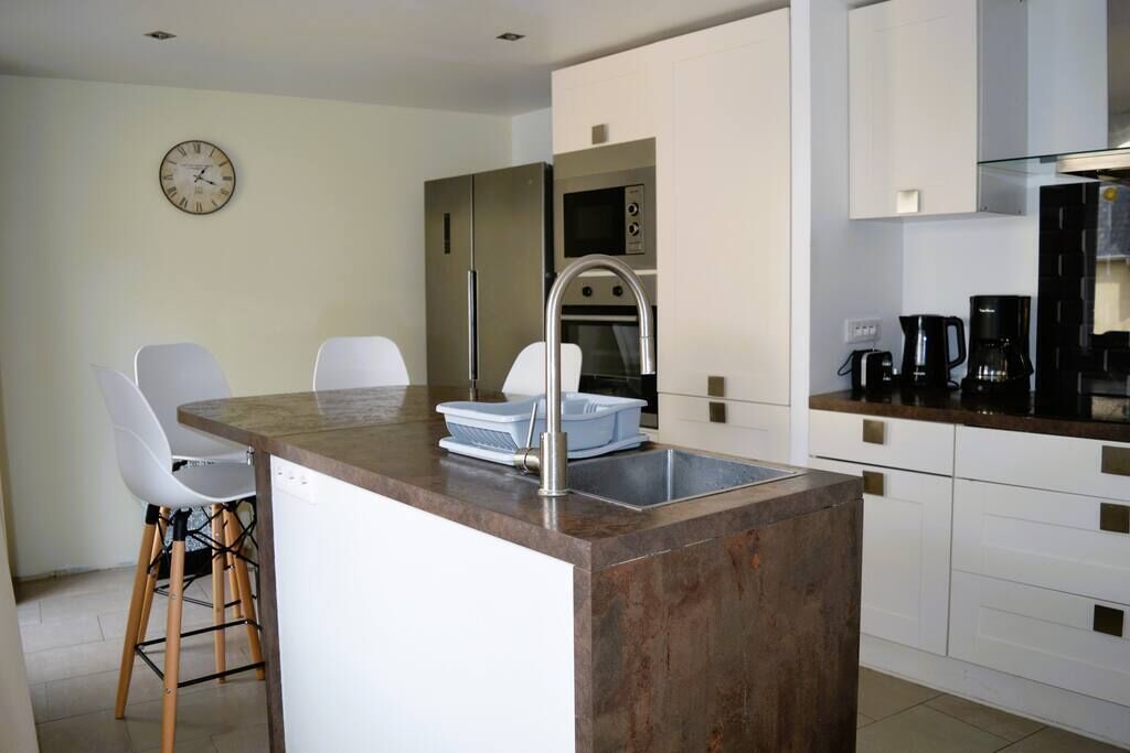 A modern kitchen with a central island, white cabinets, stainless steel appliances, and a clock on the wall.