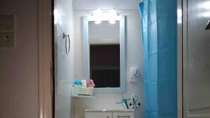 Une petite salle de bain avec un rideau de douche, un miroir, un lavabo et un tapis sur le sol.