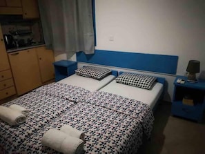 Un lit double avec une literie à motifs, une table de chevet avec une lampe et un petit coin cuisine équipé d’une bouilloire.