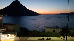 Une vue sur la côte au crépuscule, avec une silhouette de montagne bien visible, une mer calme et des immeubles résidentiels au premier plan.