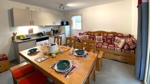 A compact kitchen with white cabinets, a microwave, and a sink. There is a dining table set with plates, glasses, and cutlery. A wooden bench and a sofa with patterned cushions are in the living area.