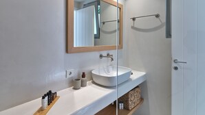 Un baño moderno con un lavamanos blanco, un espejo con marco de madera y una cabina de ducha de vidrio.