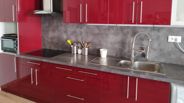 A modern kitchen with red cabinets, a stainless steel sink, and a built-in oven.