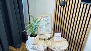 A modern room with a wooden slat wall, a black floor lamp, a small round table with a potted plant, a framed welcome sign, and a small sign with a name. - Fewo Haus ,,eckernförde (Schönberg)