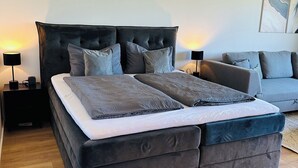 A modern bedroom with a large bed, a grey sofa, and a wooden floor. - Fewo Haus ,,eckernförde (Schönberg)