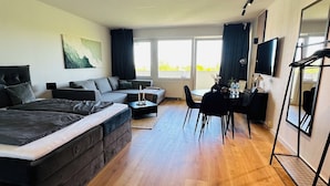 A modern hotel room with a large bed, a desk, and a dining area. - Fewo Haus ,,eckernförde (Schönberg)