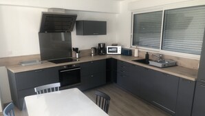 Eine moderne Küche mit Einbauofen, Mikrowelle und Spüle. Ein Esstisch mit Stühlen und ein Fenster mit Jalousien sind ebenfalls vorhanden.
