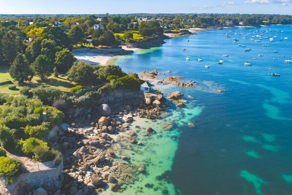 An aerial view of a coastal area with rocky shores, clear blue waters, and numerous boats. - Ground-floor Apartment B (3-room) with a terrace near the beach (Fouesnant)