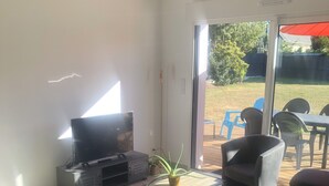 Ein modernes Wohnzimmer mit einem Flachbildfernseher, bequemen Sitzmöglichkeiten und einer Schiebetür zu einer Außenpatiofläche.